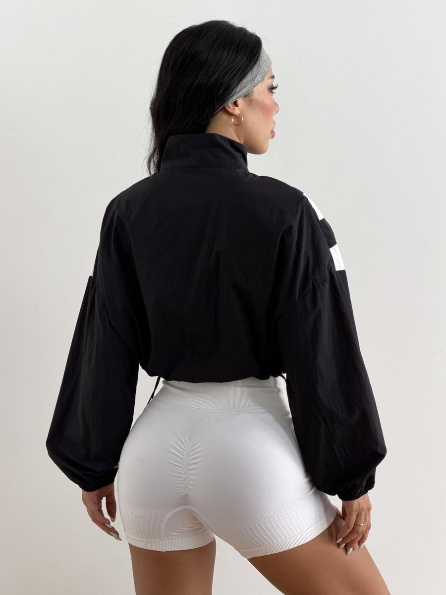 Black cropped lightweight sports jacket for women featuring colorblock stripes, a funnel neck, long sleeves, and a zipper closure.